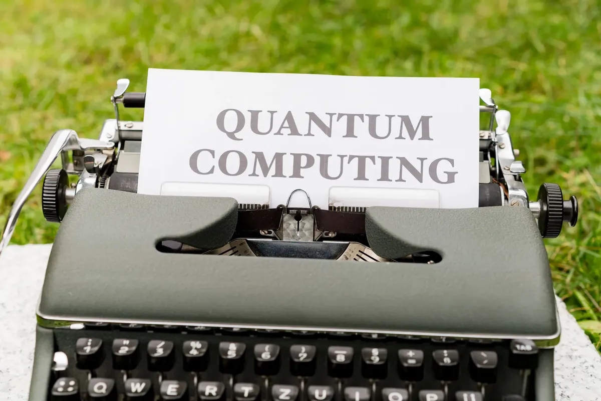A typewriter with 'Quantum Computing' text outdoors on grass, blending old and new technologies.